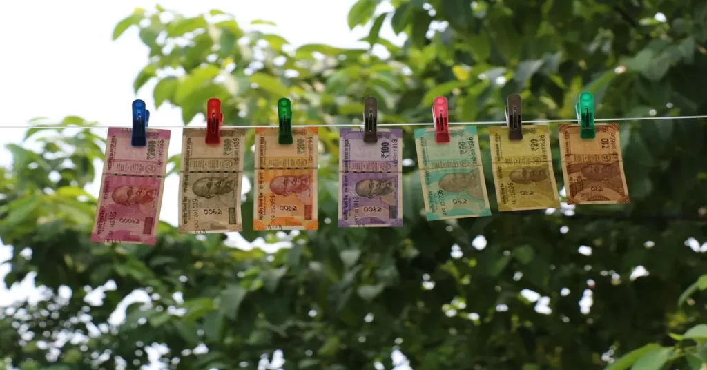 Indian rupee banknotes clipped and hanging on a rope outdoors.