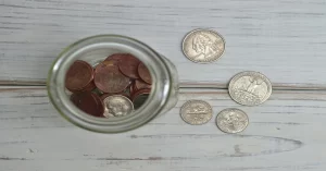 Top view of coins stored in a glass jar with several loose coins placed beside it.