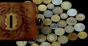 Collection of assorted coins near a vintage wooden piggy bank box.